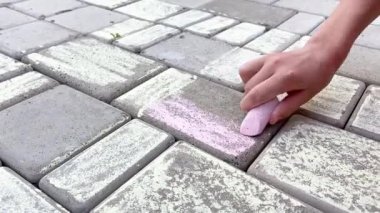Çömelmiş bir kız kaldırım taşlarına tebeşirle çiziyor. Yakın çekim görünümü 