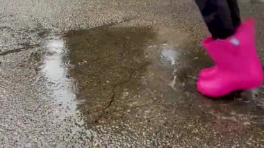 Pembe çizmeli bir çocuk su birikintisine atlıyor. 