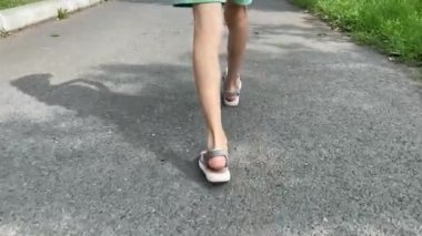 Sandaletli bir çocuk asfaltta yürüyor. Bacaklarını kapat. 