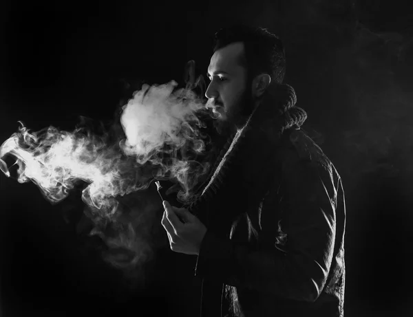 Homem barbudo elegante segurando e fumando cigarro eletrônico — Fotografia de Stock