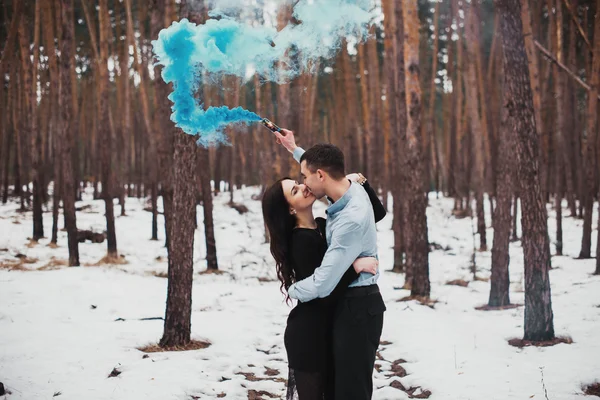 Pár objímat v zimním lese s barevný kouř — Stock fotografie