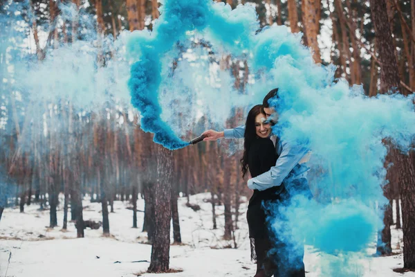 Pareja abrazándose en el bosque de invierno con humo de color — Foto de Stock