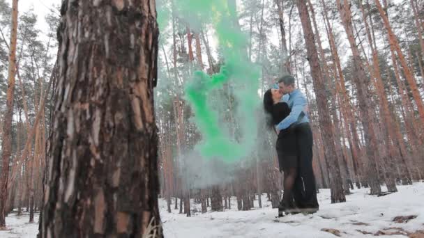 对有颜色的夫妇在冬季森林抽烟。颜色的炸弹。亲吻和拥抱 — 图库视频影像