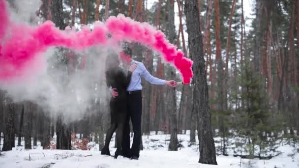 Пара с цветным дымом в зимнем лесу. Цветная бомба. целоваться и обниматься — стоковое видео