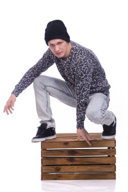 Kameraya bir büyüleyici samimi gülümseme ile beyaz stüdyo arka plan üzerinde arıyorsunuz bir ahşap kutu üzerinde oturan trendy seksi yakışıklı genç