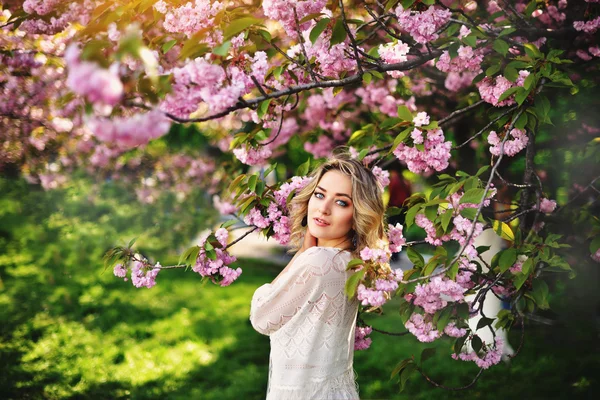 Chica de belleza de primavera con el pelo largo y rojo soplado al aire libre. Árbol de sakura floreciente. Retrato romántico de mujer joven — Foto de Stock