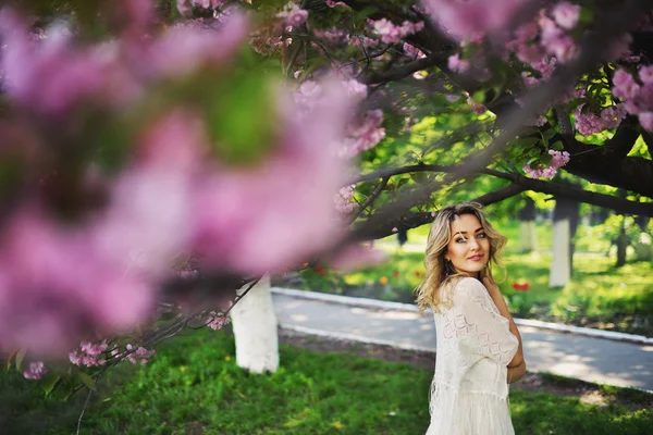 Vårens skönhet flicka med långa röda blåser håret utomhus. Blommande sakura träd. Romantiska ung kvinna porträtt — Stockfoto