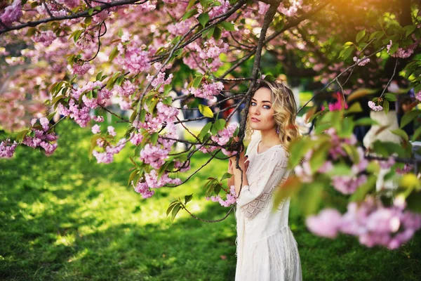 Vårens skönhet flicka med långa röda blåser håret utomhus. Blommande sakura träd. Romantiska ung kvinna porträtt — Stockfoto