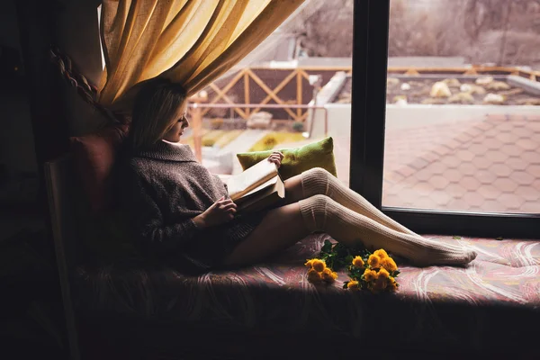 Retrato de mujer hermosa joven en jersey gris sentado en el alféizar de la ventana con libro — Foto de Stock