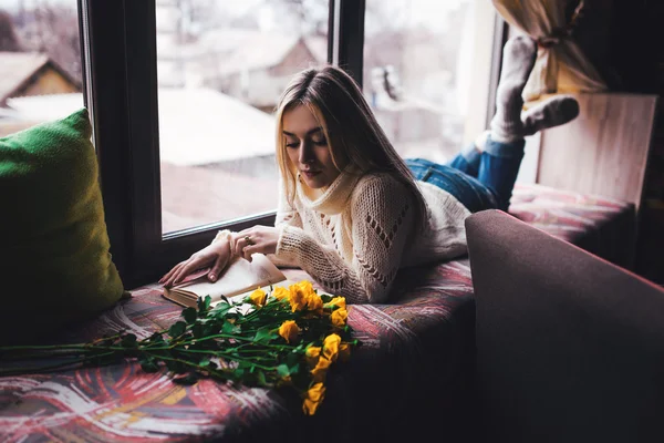 Retrato de mujer hermosa joven en jersey gris sentado en el alféizar de la ventana con flores amarillas — Foto de Stock