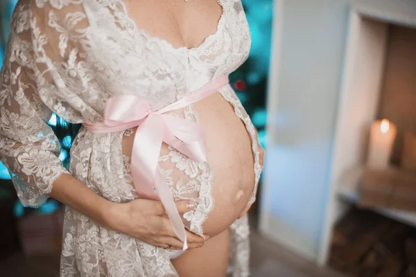 Nahaufnahme einer schwangeren Frau, die vor Kamin und Weihnachtsbaum posiert — Stockfoto