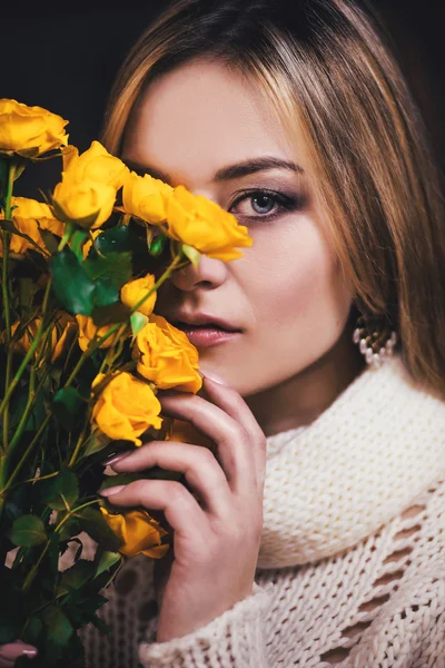 Een close-up portret van een jong meisje met gele roos in de buurt van haar gezicht, op donkere achtergrond. Mode foto. — Stockfoto