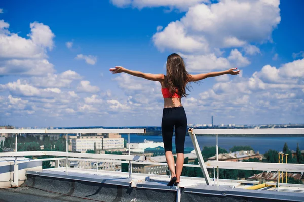 Retrato de una mujer rubia fuerte en ropa deportiva haciendo ejercicio estirándose en el techo del rascacielos sobre la gran ciudad a primera hora de la mañana. Cuerpo muscular deportivo y sexy femenino. Concepto Fitness . — Foto de Stock