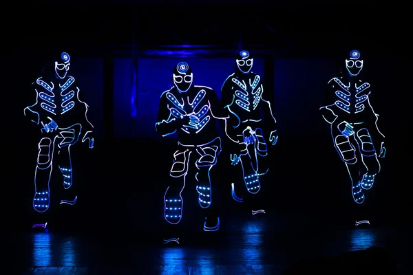 Bailarines en trajes led sobre fondo oscuro, espectáculo de colores — Foto de Stock