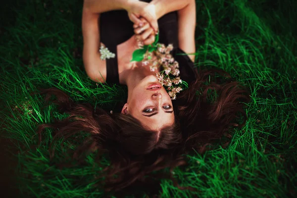 Close up retrato de jovem mulher bonita com cabelos castanhos vermelhos deitado na grama com pequenas flores brancas em torno de sua cabeça. Conceito de primavera verão felicidade dos jovens — Fotografia de Stock