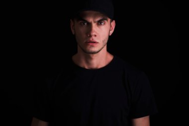 Beyzbol şapkalı yakışıklı genç adam. doğrudan kameraya ciddi görünümlü, siyah arka plan üzerine izole