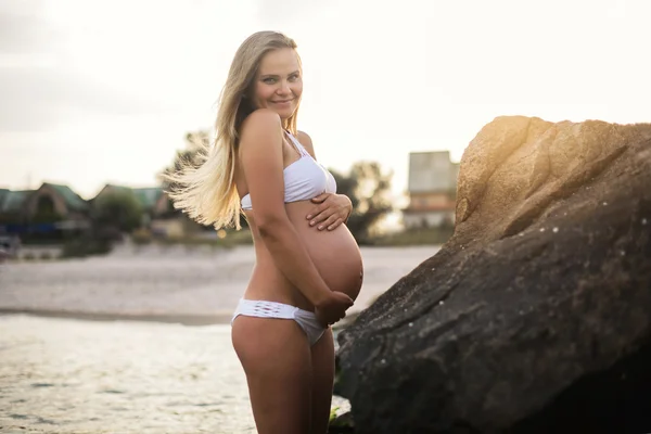 Mujer embarazada de pie cerca de las piedras en la playa — Foto de Stock