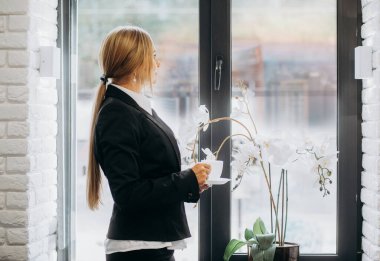 Düşünceli iş kadını kahve içiyor, büyük modern şehre bakıyor, derin düşünceler içinde, manzaranın tadını çıkarıyor, toplantının başlamasını bekliyor, iş kararı veriyor, boşluğu kopyalıyor.