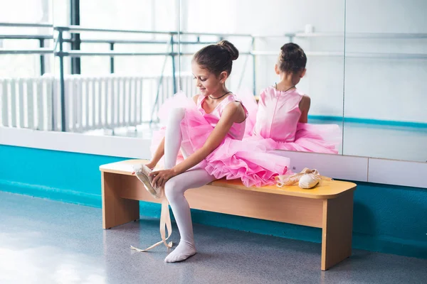 Jovem bailarina em roupas rosa sentada no banco durante o treinamento em aula de dança . — Fotografia de Stock