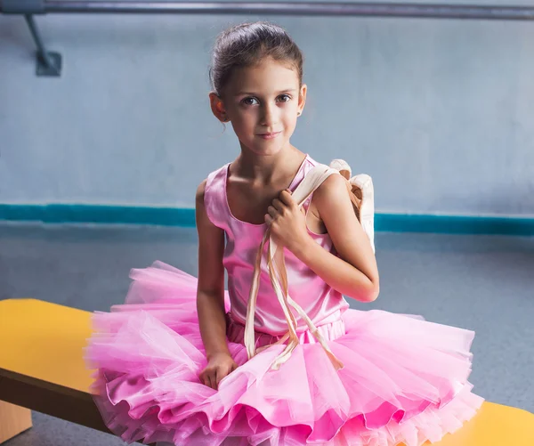 Jovem bailarina em roupas rosa sentada no banco durante o treinamento em aula de dança . — Fotografia de Stock