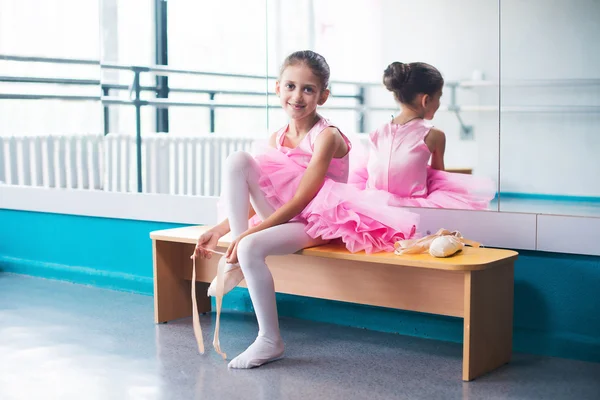 Jovem bailarina em roupas rosa sentada no banco durante o treinamento em aula de dança . — Fotografia de Stock