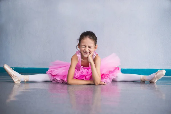 Jovem bailarina em roupas rosa sentada no chão durante o treinamento em aula de dança . — Fotografia de Stock