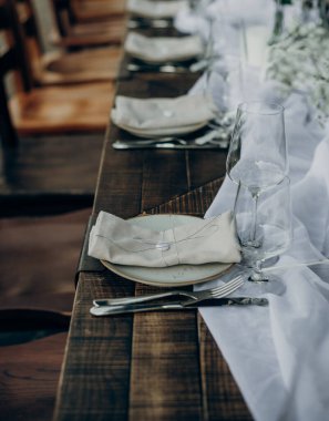 Açık hava ziyafeti için güzel bir ahşap masa. Mumlar, cam eşyalar, tabaklar ve kurumuş çiçek dallarıyla süslenmiş peçeteler..