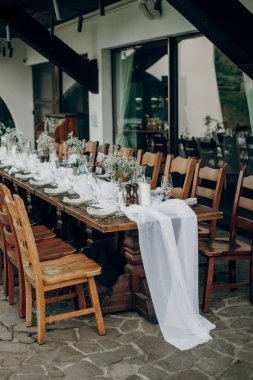 Açık hava ziyafeti için güzel bir ahşap masa. Mumlar, cam eşyalar, tabaklar ve kurumuş çiçek dallarıyla süslenmiş peçeteler..