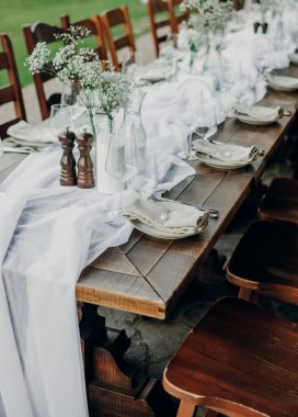 Açık hava ziyafeti için güzel bir ahşap masa. Mumlar, cam eşyalar, tabaklar ve kurumuş çiçek dallarıyla süslenmiş peçeteler..