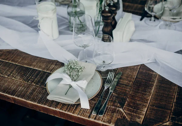 Açık hava ziyafeti için güzel bir ahşap masa. Mumlar, cam eşyalar, tabaklar ve kurumuş çiçek dallarıyla süslenmiş peçeteler..