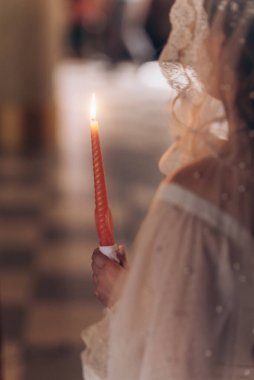 Ortodoks kilisesi ayini sırasında gelin tarafından tutulan yanan bir düğün mumunun yakın çekimi. İnancı, evliliği ve kutsal birlikteliği simgeliyor..
