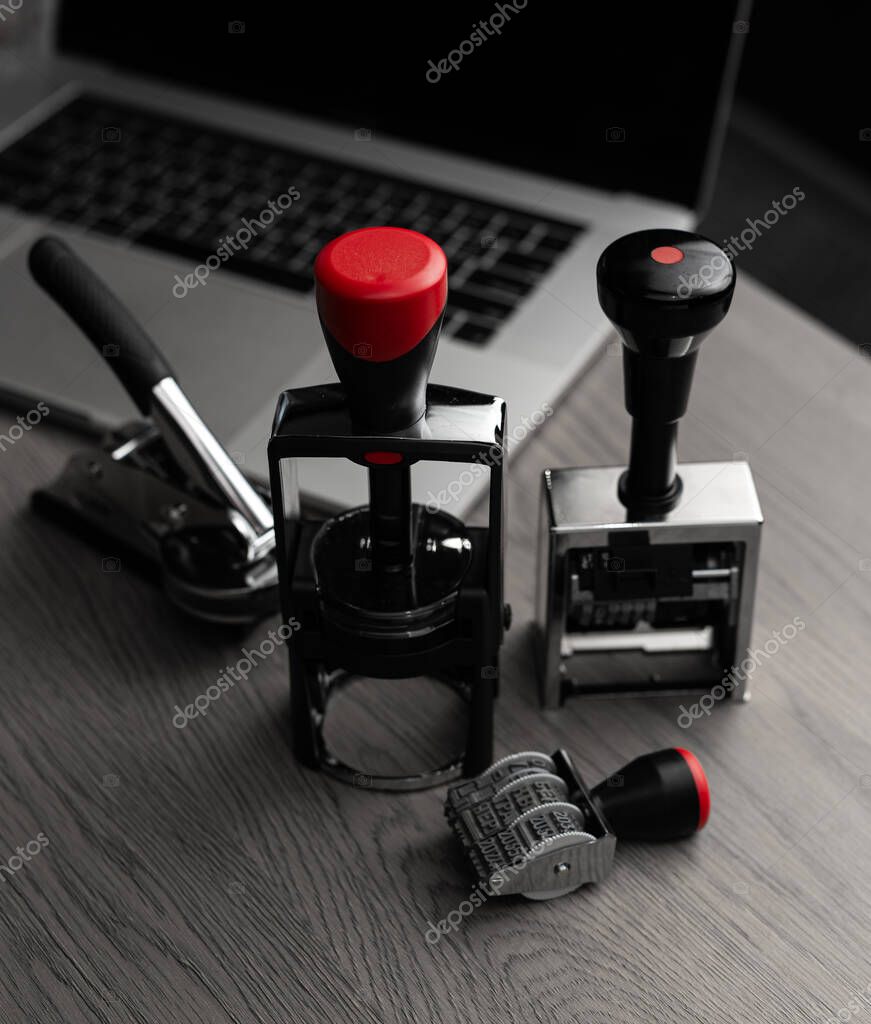 Various stamps and embossing tool on table. Concept of stamp makers, branding, and office equipment production.