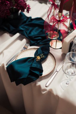 Bej masa örtüsü, altın tutacaklarda yeşil peçeteler, altın şamdanlarda kırmızı mumlar ve seramik tabaklar. Rafine edilmiş yemek dekoru..