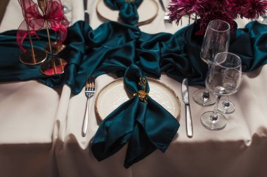 Bej masa örtüsü, altın tutacaklarda yeşil peçeteler, altın şamdanlarda kırmızı mumlar ve seramik tabaklar. Rafine edilmiş yemek dekoru..