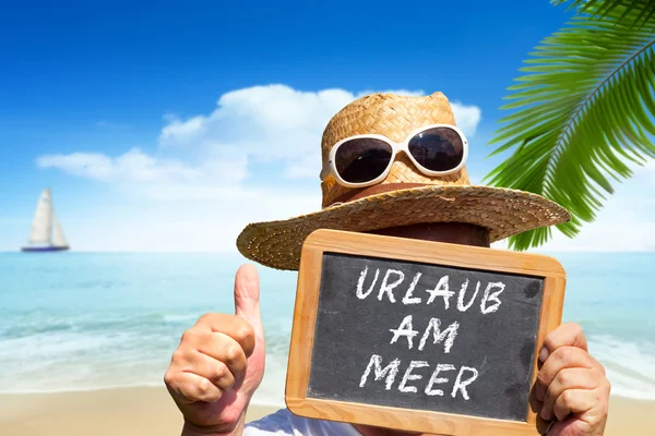 L'uomo mostra lavagna ardesia con messaggio di testo "Urlaub am Meer " — Foto Stock