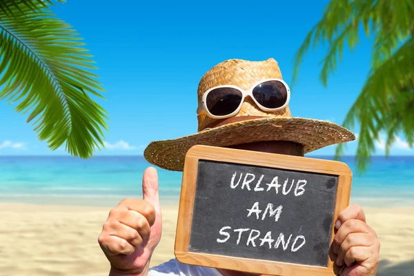 Hombre muestra pizarra pizarra con mensaje de texto "Urlaub am Strand " —  Fotos de Stock