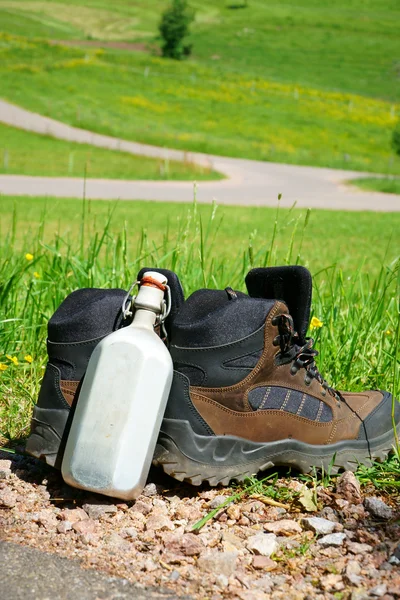 Botas de caminhada em frente a um prado de verão — Fotografia de Stock