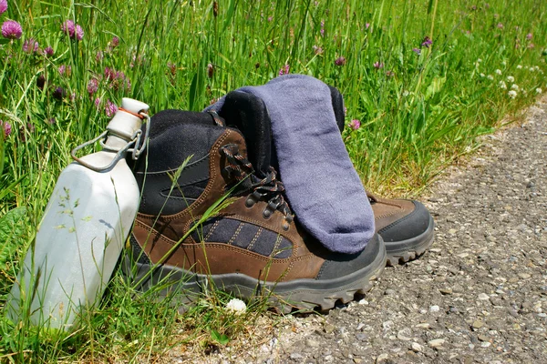 Botas de caminhada em frente a um prado de verão — Fotografia de Stock