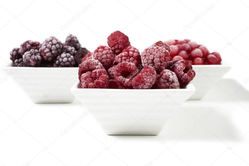 Bowls with frozen berries on white background