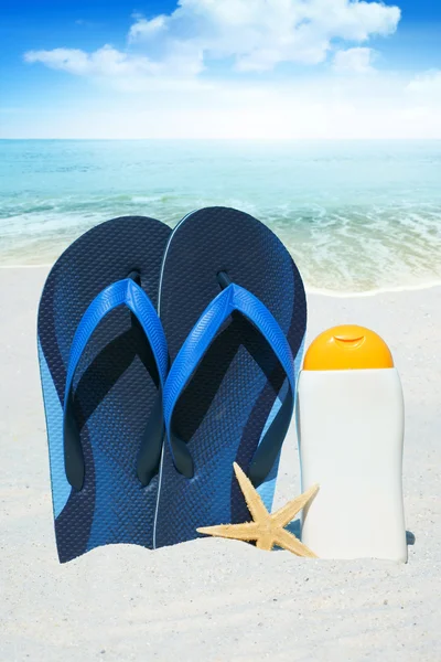 Chanclas y crema solar en la playa — Foto de Stock