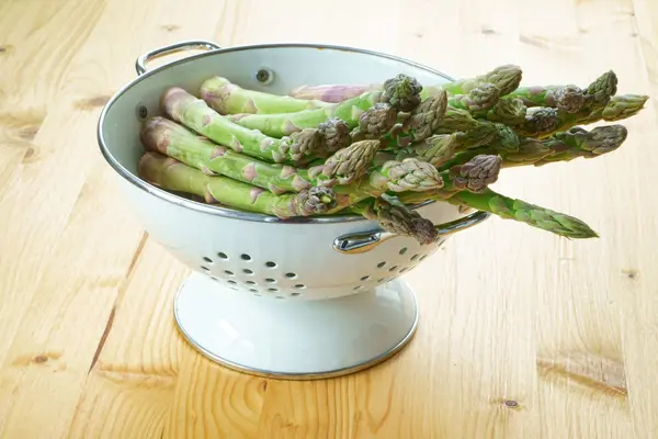 Asparagus in a white enamel colander — Stock Photo, Image