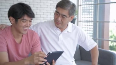 Aile kavramı. Asyalı oğul ve baba oturma odasında tablet oynarken eğleniyorlar. 4k Çözünürlüğü.