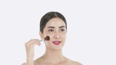 Güzellik konsepti. Asyalı kadınlar beyaz arka planda makyaj fırçalarıyla yanaklarını fırçalıyorlar. 4k Çözünürlüğü.