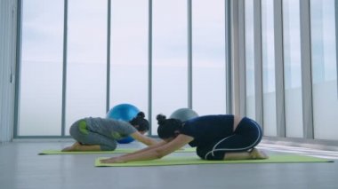 Egzersiz konsepti. Bir grup kadın yoga minderinde bir öğretmenle balasana egzersizi yapıyor. 4k Çözünürlüğü.