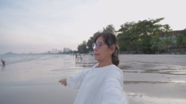 Tatil konsepti 4k Çözünürlük. Asyalı yaşlı bir kadın kumsalda mutlu bir şekilde nefes alıyor..