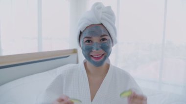 Spa konsepti 4k Çözünürlük. Asyalı kız yatak odasında gözlerine salatalık sürüyor..