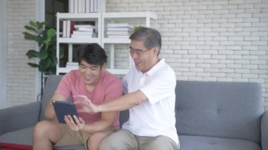 Aile kavramı 4k Kararlılığı. Asyalı bir oğul ve baba oturma odasındaki televizyonun keyfini çıkarıyor..