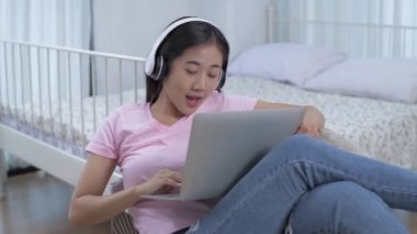Ev konsepti olan 4k çözünürlük üzerinde çalış. Yatak odasında bilgisayar oynayan Asyalı genç kadın..