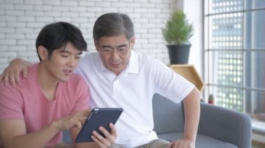 Aile kavramı 4k Kararlılığı. Asyalı oğul ve baba oturma odasında tablet oynarken eğleniyorlar..