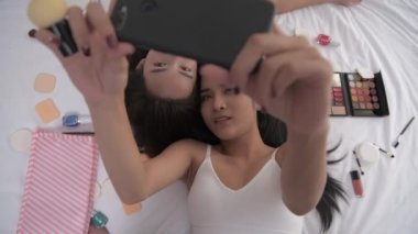 4k Çözünürlük 'ün güzellik konsepti. Asyalı kızlar yatak odasında makyaj yaparken cep telefonuyla fotoğraf çekiyorlar..